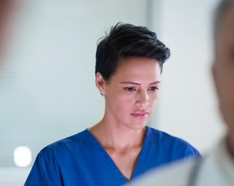 Female doctor wearing blue scrubs looking at computer with other doctors in the room