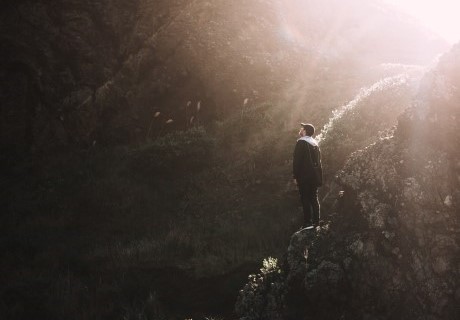 Stock photo of a hiker on a mountain looking up at the ray of sunbeam shining through.