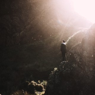 Stock photo of a hiker on a mountain looking up at the ray of sunbeam shining through.